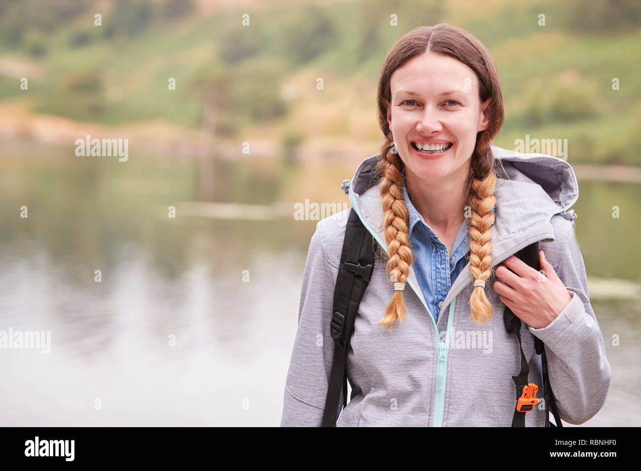 Young adult woman on a camping holiday standing by a lake laughing, portrait, Lake District, UK Stock Photo
