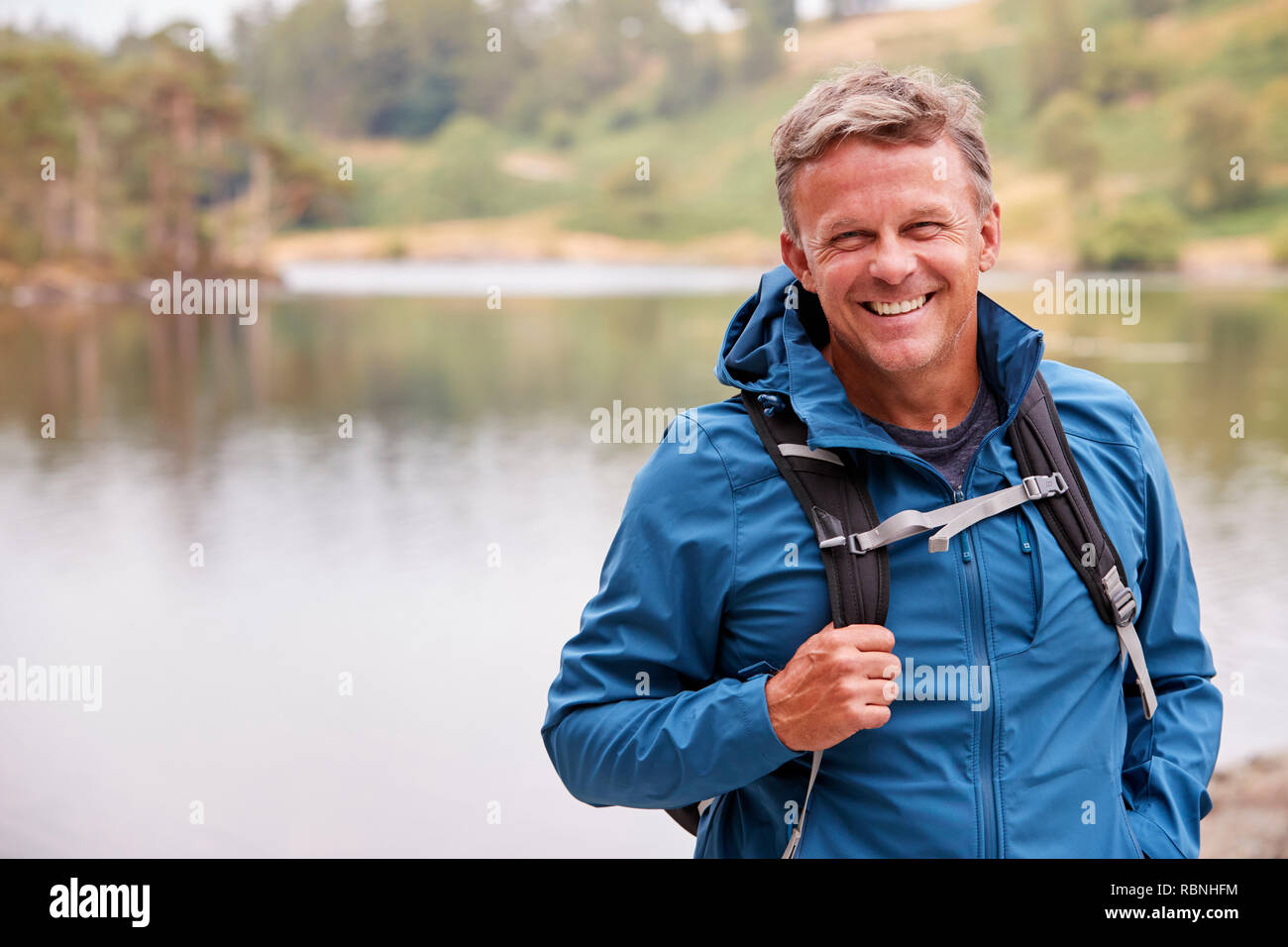 Adult man on a camping holiday standing by a lake smiling to camera, close up, Lake District, UK Stock Photo