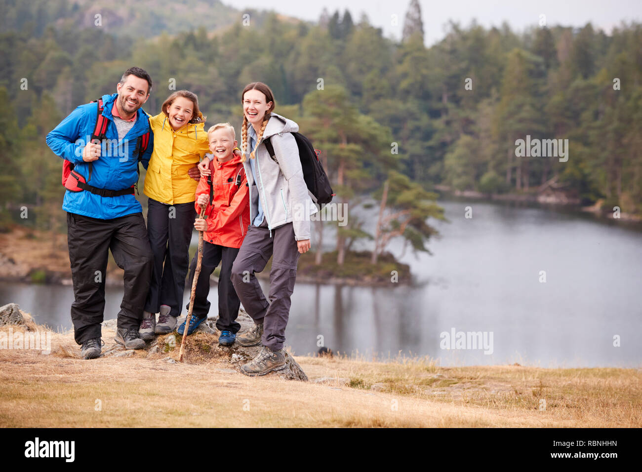 Young family standing on a rock by a lake looking to camera embracing, full length Stock Photo