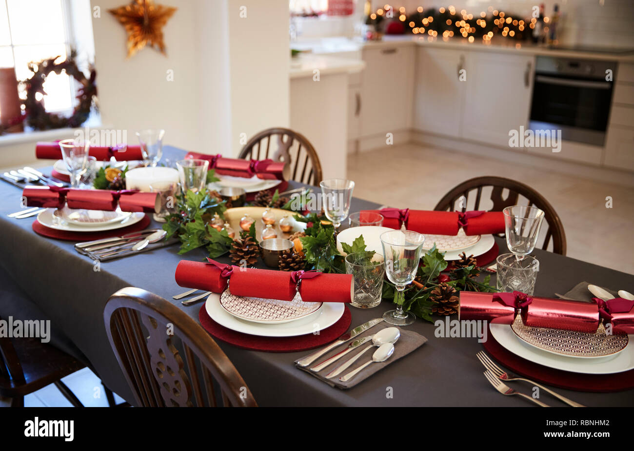 Christmas table setting with Christmas crackers arranged on plates in a dining room, with kitchen in the background Stock Photo