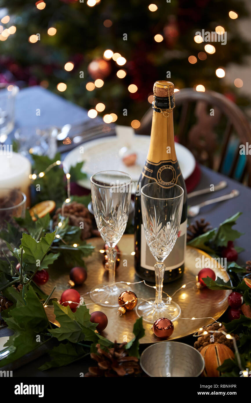 Christmas table setting with glasses and a bottle of champagne, baubles arranged on a gold plate and green and red table decorations, vertical Stock Photo