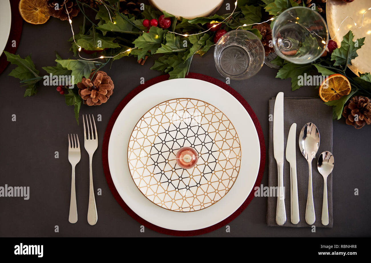 Christmas table place setting with bauble arranged on a plate and green and red table decorations, overhead view Stock Photo
