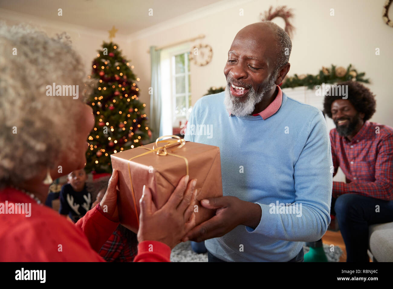 Senior Couple Exchanging Gifts As They Celebrate Christmas At Home With Family Stock Photo