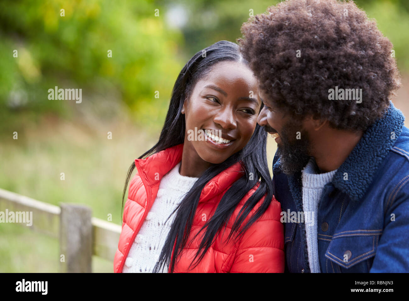 Happy black couple leaning on a fence in the countryside looking into each other’s eyes, close up Stock Photo