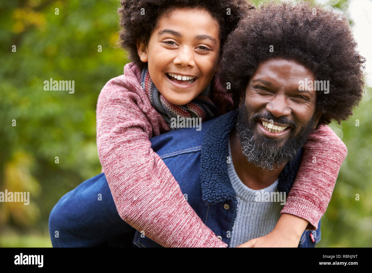 Black man piggybacking his pre-teen son in the park, both smiling to camera, close up Stock Photo