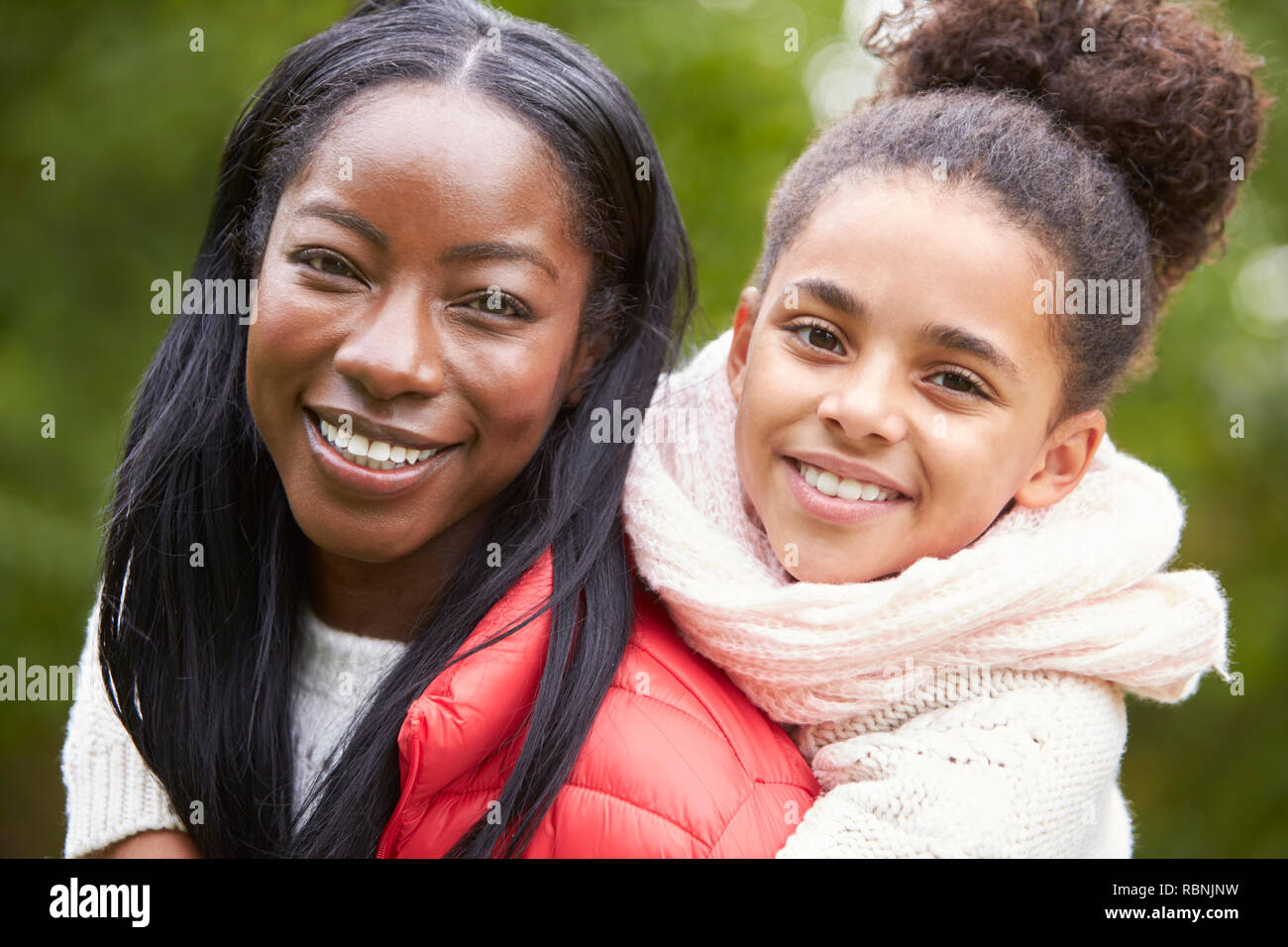 Young black woman piggybacking her pre-teen daughter in the park, both smiling to camera, close up Stock Photo