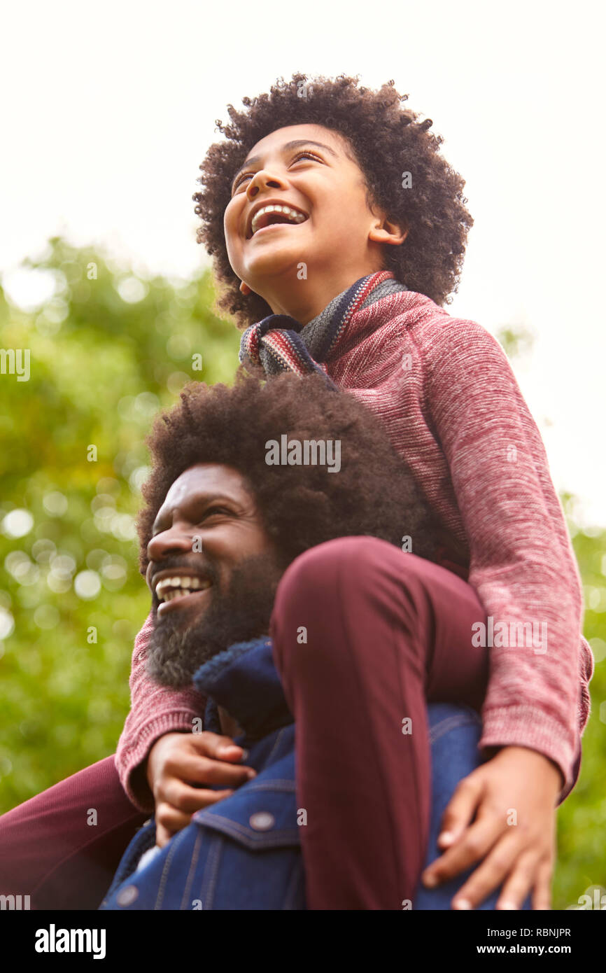 Black middle aged man carrying his son on his shoulders in the park, close up, low angle Stock Photo