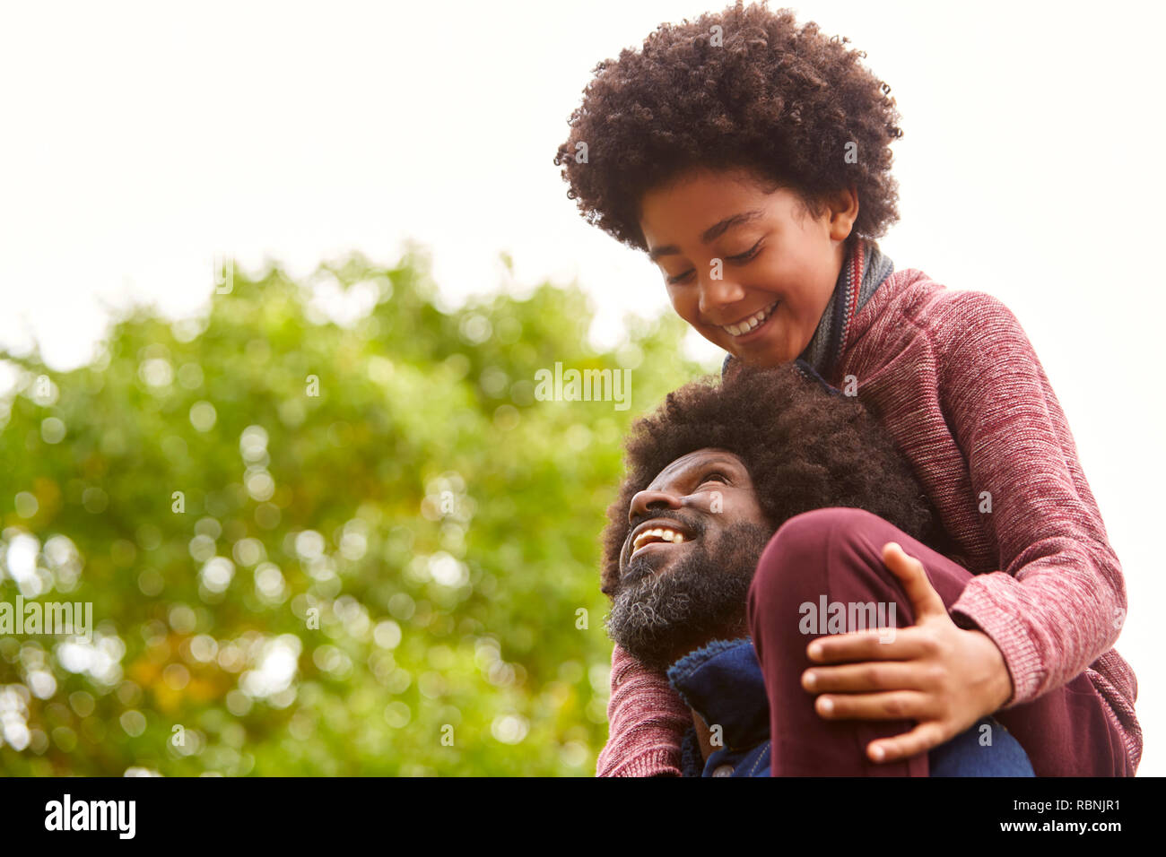 Black middle aged man carrying his son on his shoulders in the park looking at each other, close up, low angle Stock Photo