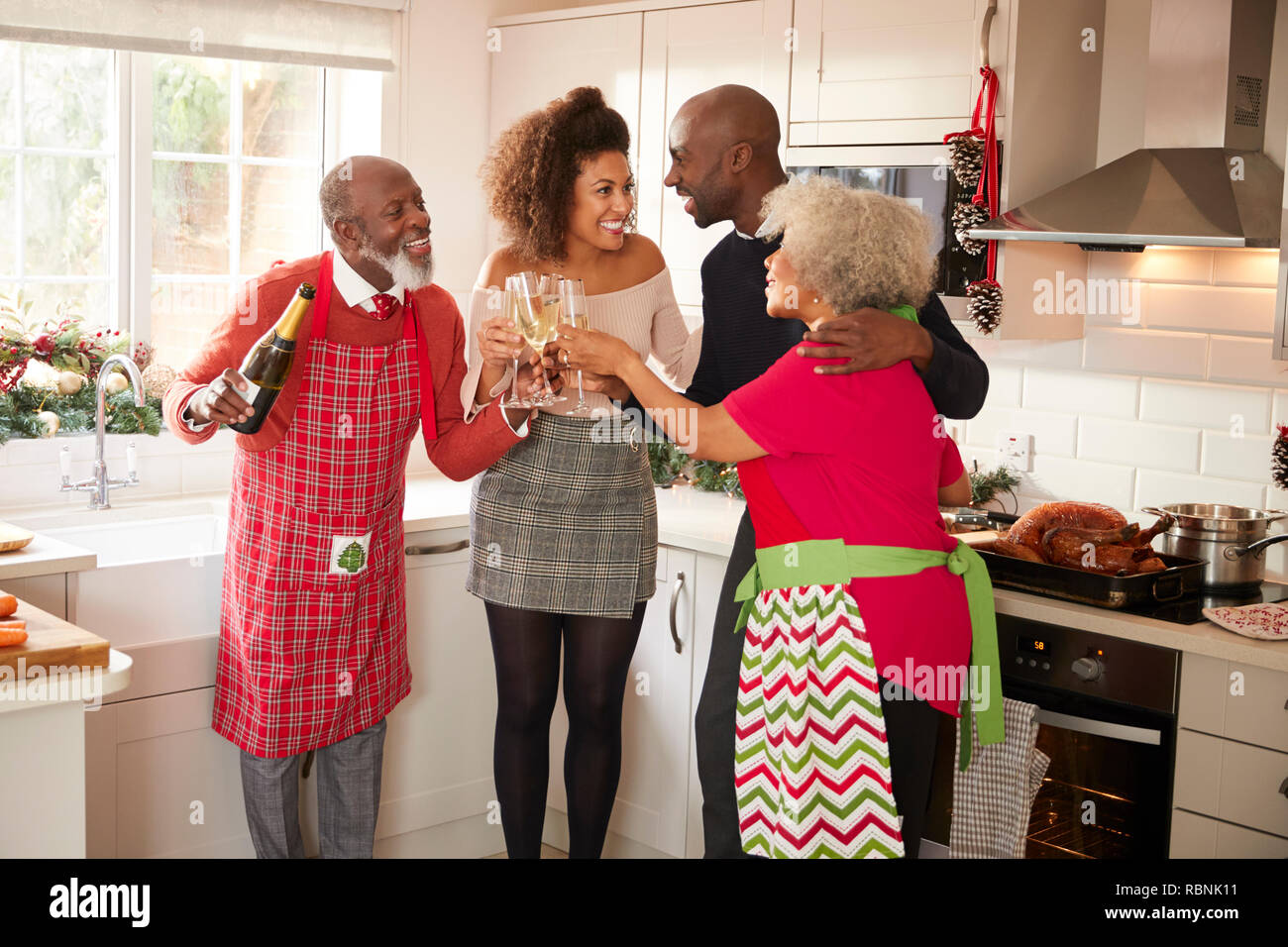 Multi-ethnic adult family embrace and make a toast with champagne to celebrate on Christmas Day while preparing dinner together in the kitchen Stock Photo