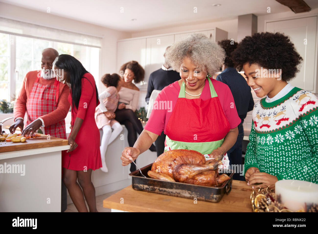 Mixed race, multi generation family gathered in kitchen before Christmas dinner, grandmother and grandson preparing roast turkey in foreground Stock Photo