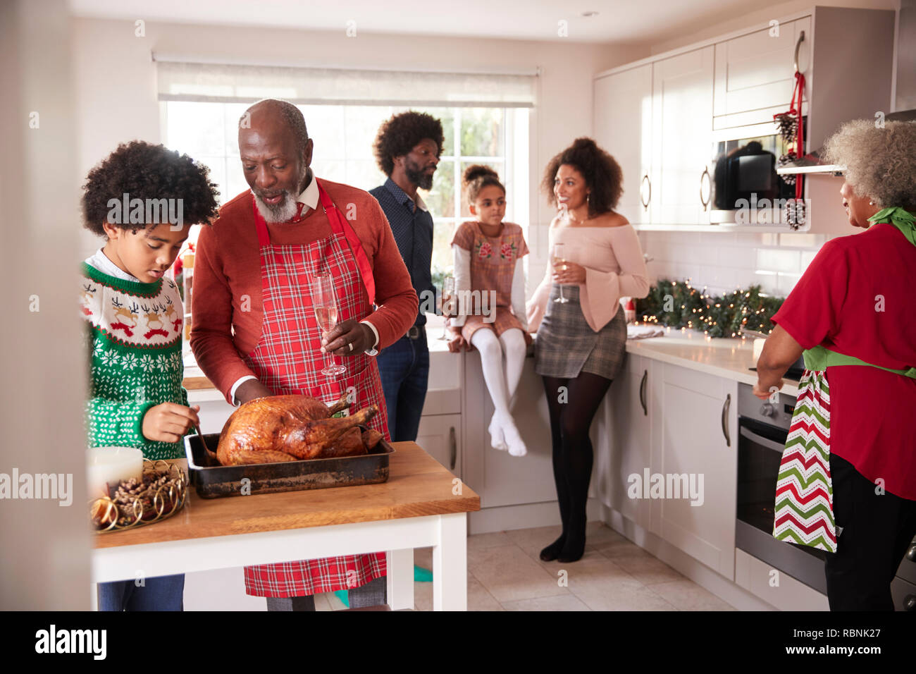 Mixed race, multi generation family gathered in kitchen before Christmas dinner, grandfather and grandson preparing roast turkey in foreground Stock Photo