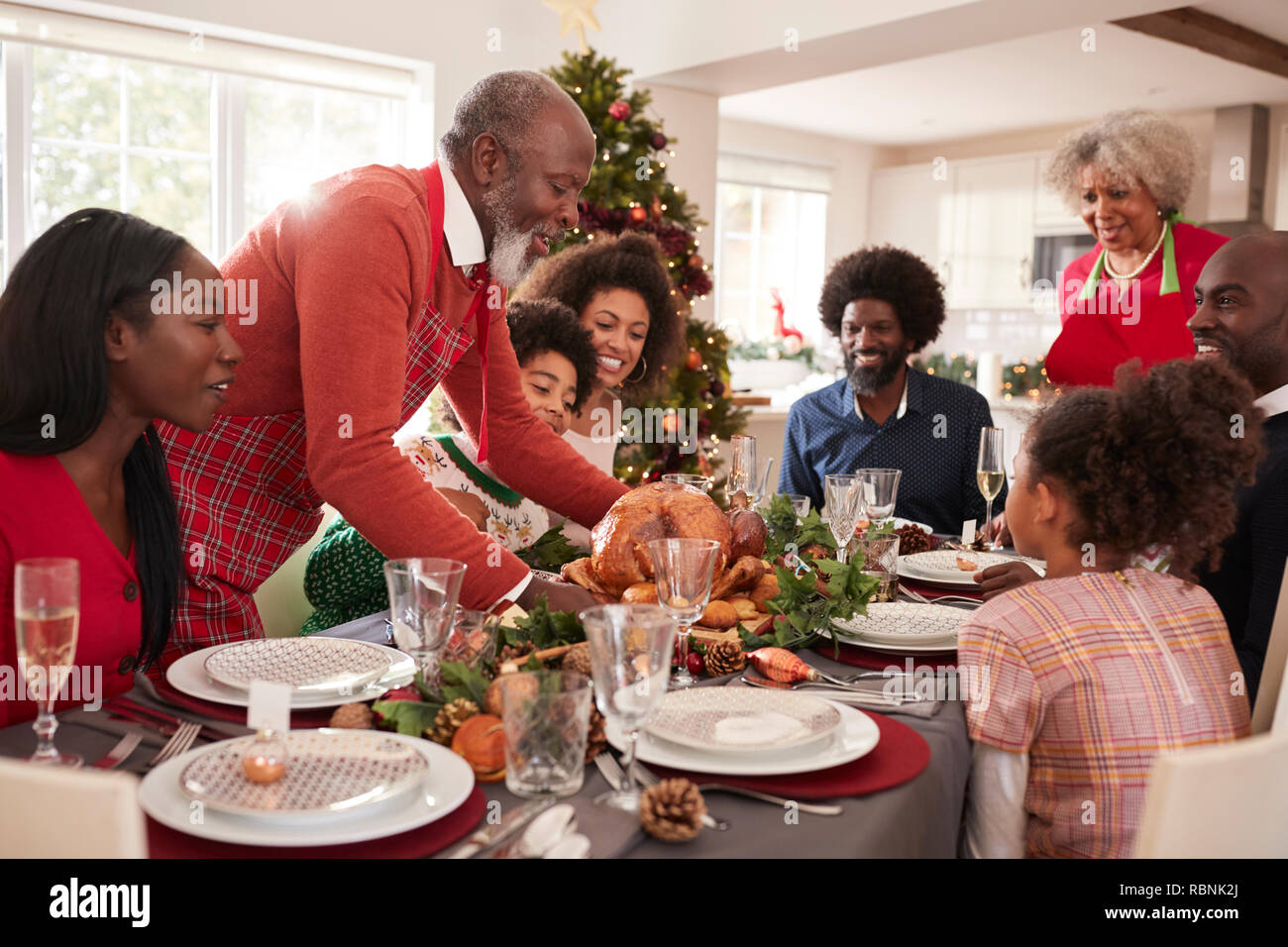 Grandfather bringing the roast turkey to the dinner table during a multi generation, mixed race family Christmas celebration, close up Stock Photo