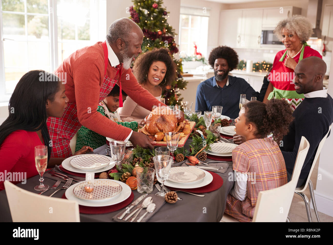 Grandfather bringing the roast turkey to the dinner table during a multi generation, mixed race family Christmas celebration, elevated view Stock Photo