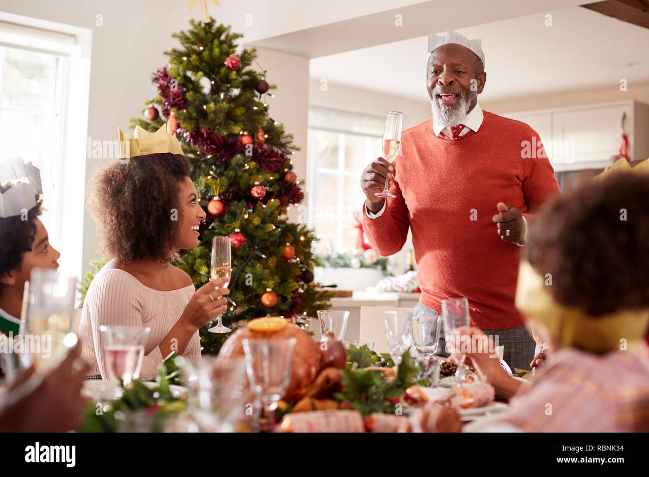 Black grandfather standing to make a speech and a toast at the head of the family Christmas dinner table, front view Stock Photo
