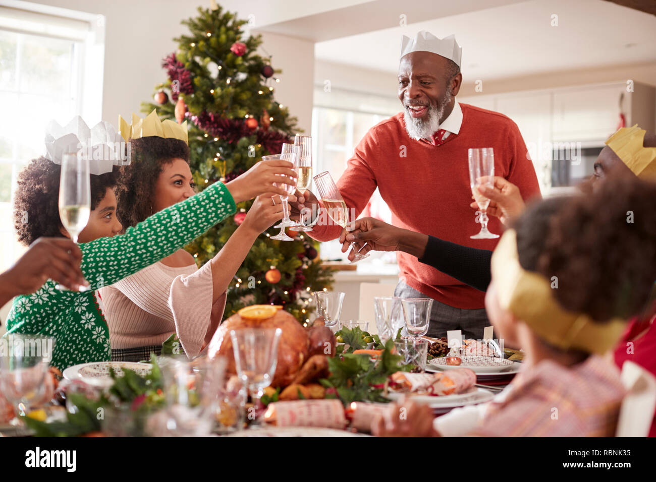 Black grandfather standing to make a toast at the head of the family Christmas dinner table, front view Stock Photo