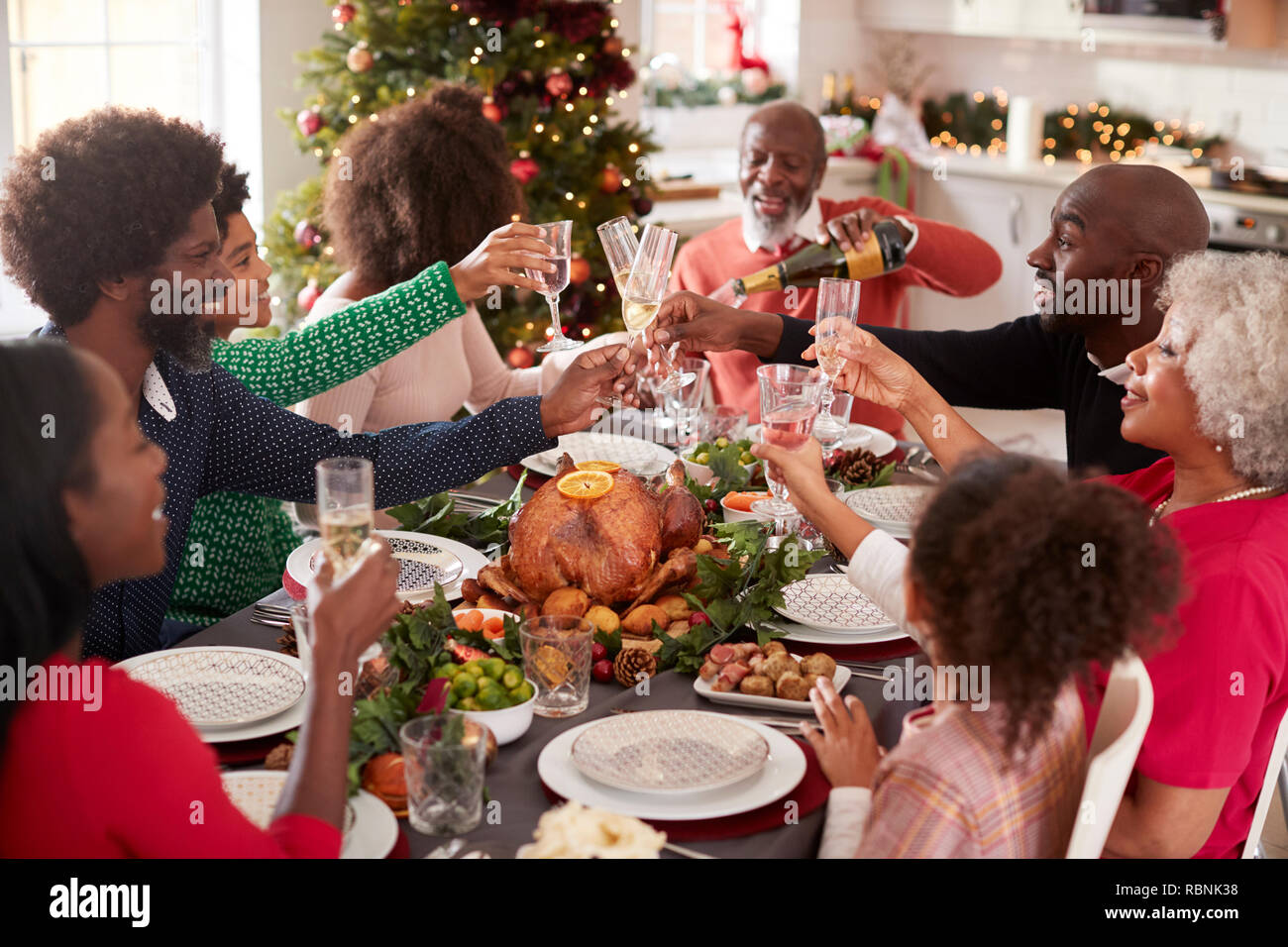 Multi generation mixed race family pouring champagne and raising glasses to make a toast sitting at the Christmas dinner table, elevated view Stock Photo