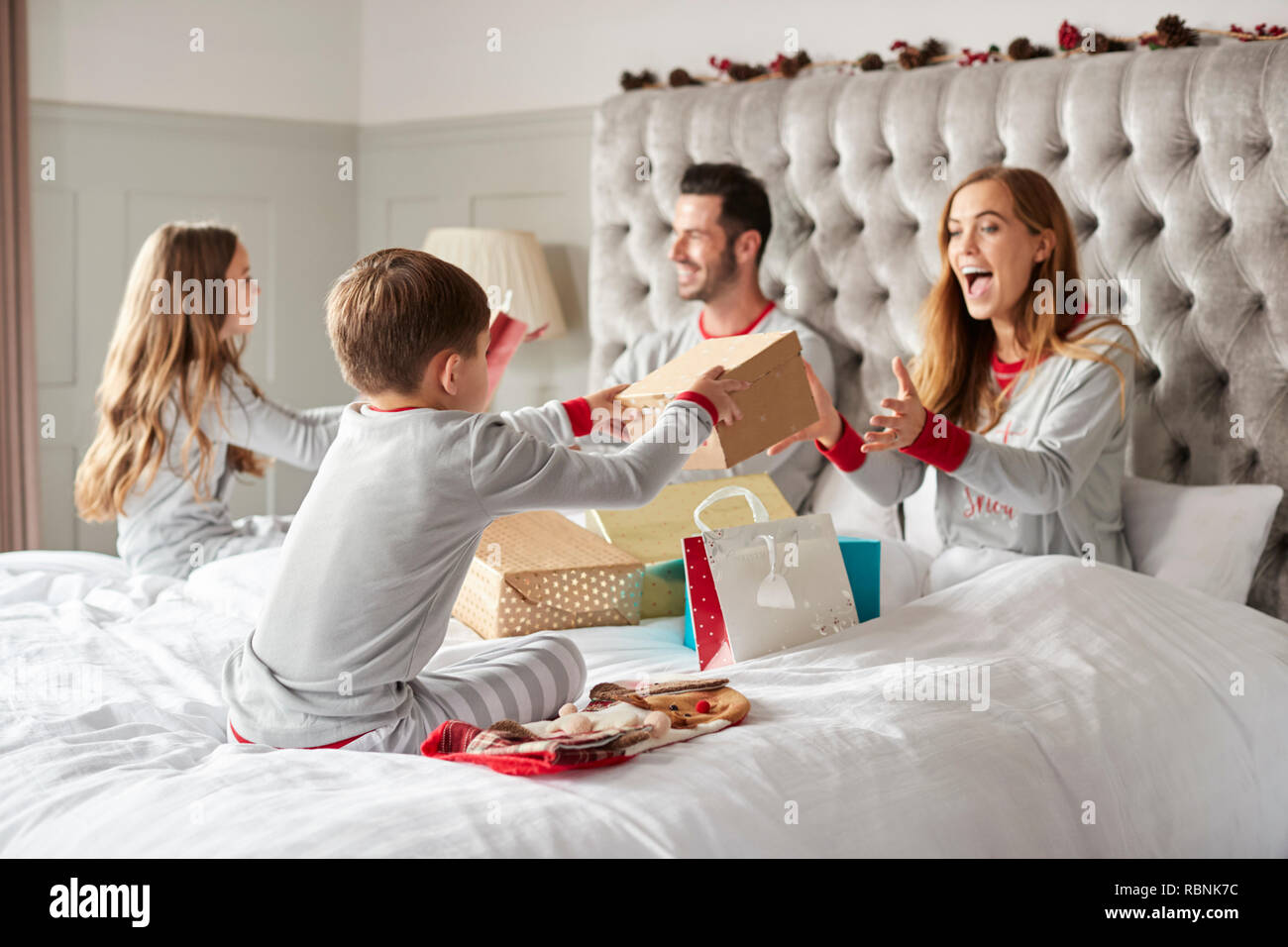 Parents Opening Gifts From Children As They Sit On Bed Exchanging Present On Christmas Day Stock Photo