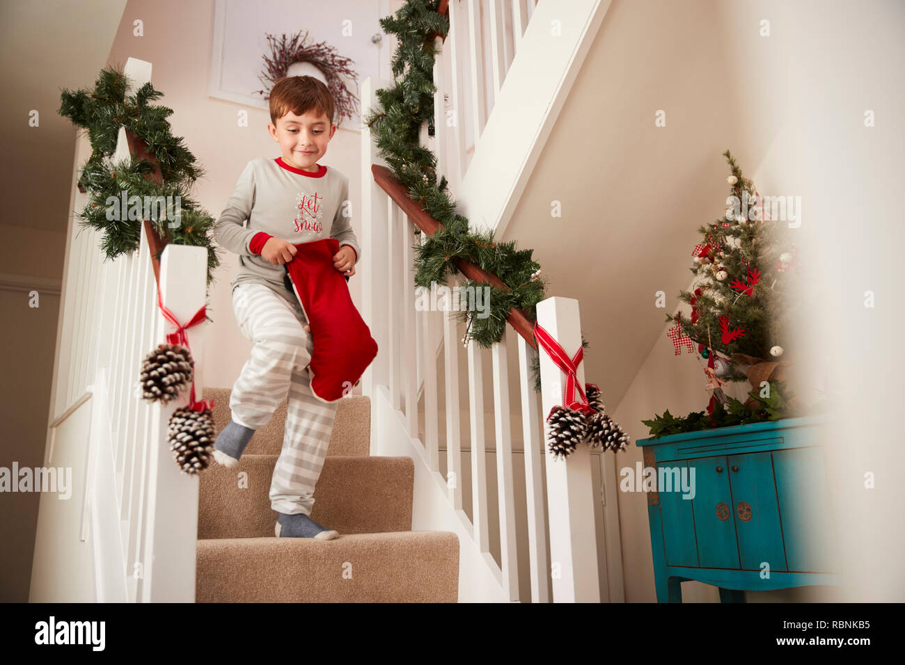 Excited Boy Wearing Pajamas Running Down Stairs Holding Stocking On Christmas Morning Stock Photo