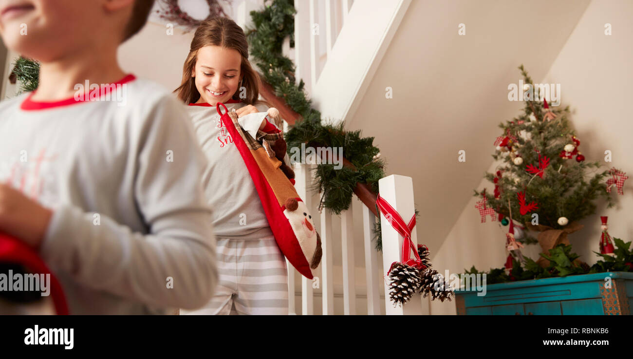 Two Excited Children Wearing Pajamas Running Down Stairs Holding Stockings On Christmas Morning Stock Photo