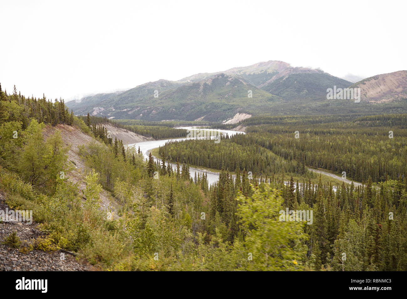 River Running Through Wooded Valley Between Mountains In Alaska Stock Photo