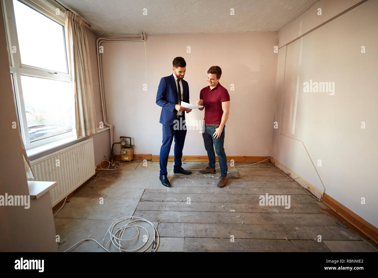 Male First Time Buyer Looking At House Survey With Realtor Stock Photo