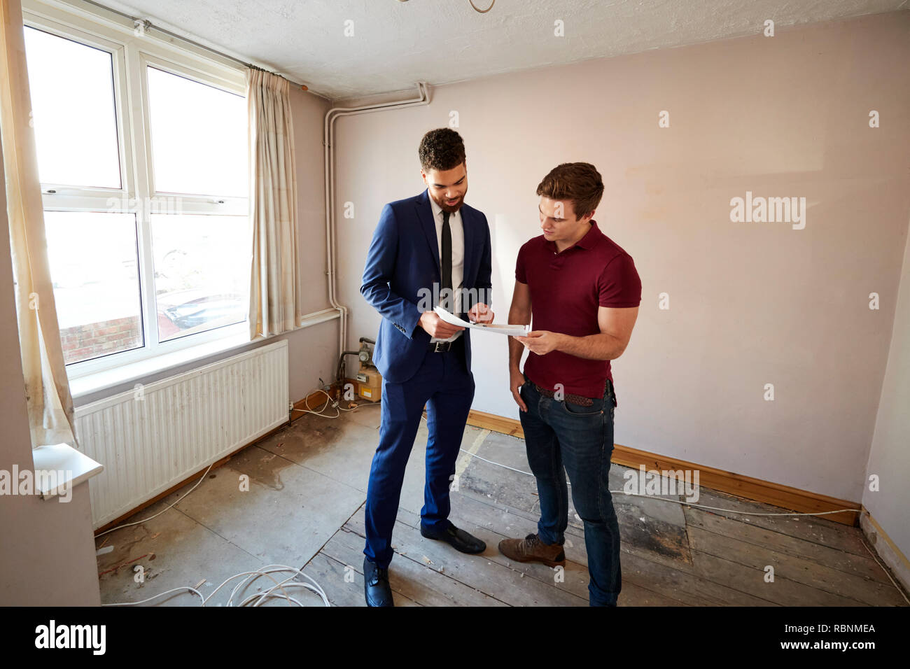 Male First Time Buyer Looking At House Survey With Realtor Stock Photo