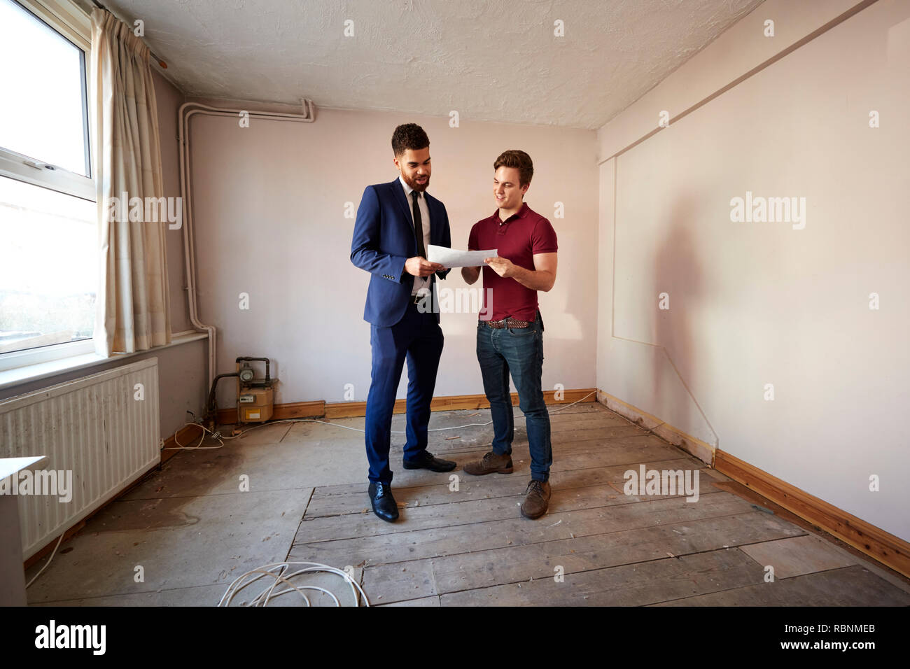 Male First Time Buyer Looking At House Survey With Realtor Stock Photo