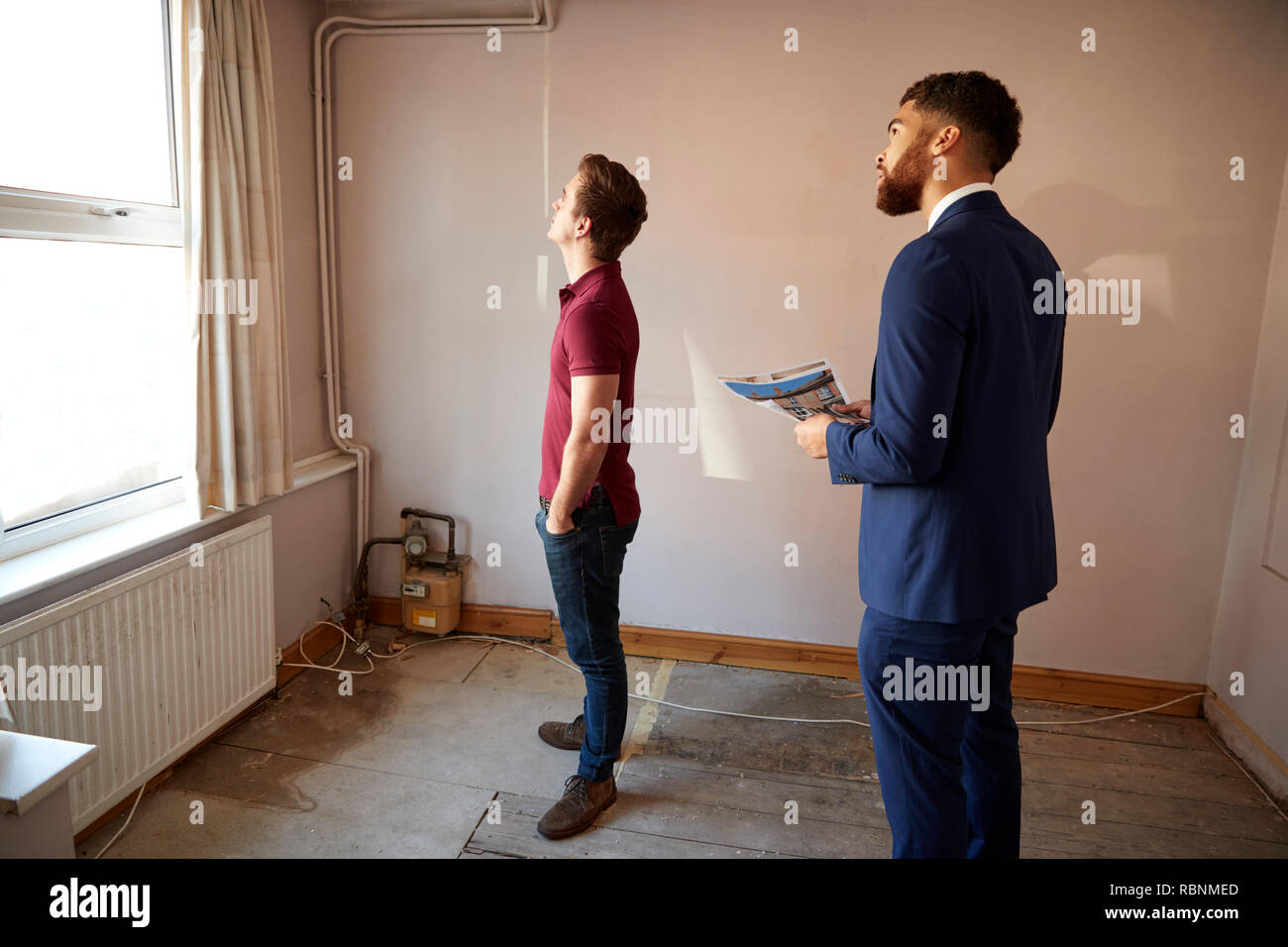 Male First Time Buyer Looking Around House For Renovation With Realtor Stock Photo