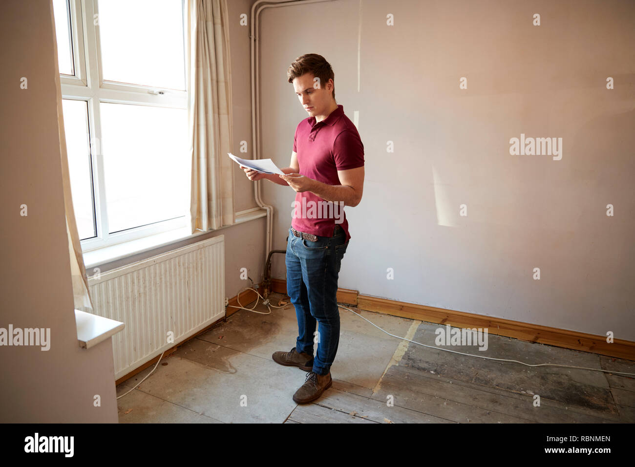 Male First Time Buyer Looking At House Survey In Room To Be Renovated Stock Photo