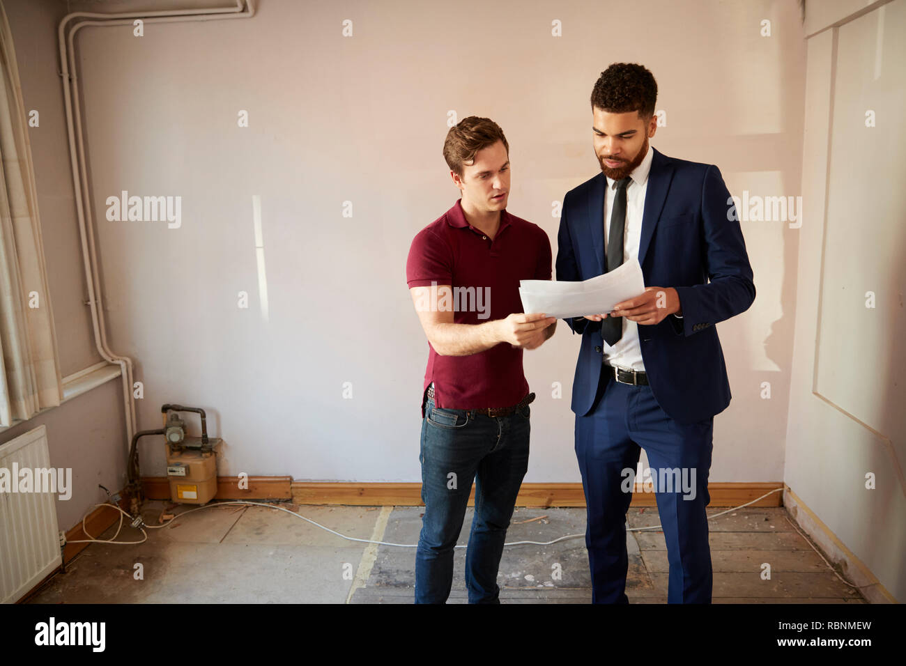 Male First Time Buyer Looking At House Survey With Realtor Stock Photo