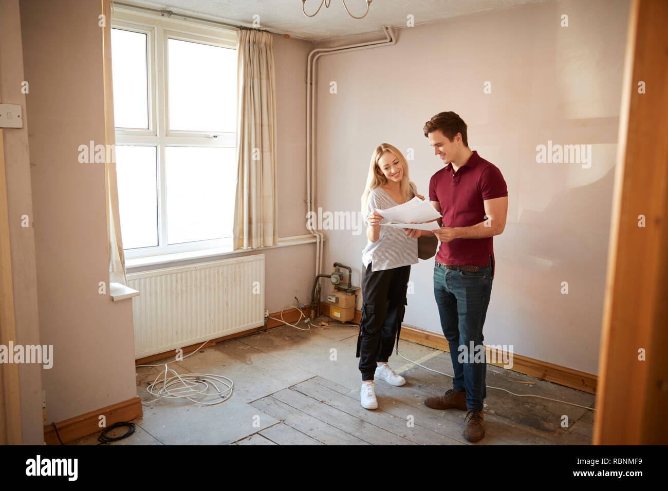 Couple Buying House For First Time Looking At House Survey In Room To Be Renovated Stock Photo