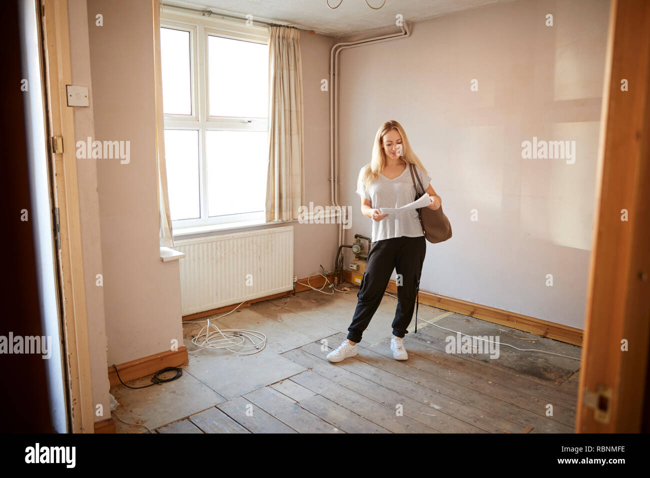 Female First Time Buyer Looking At House Survey In Room To Be Renovated Stock Photo