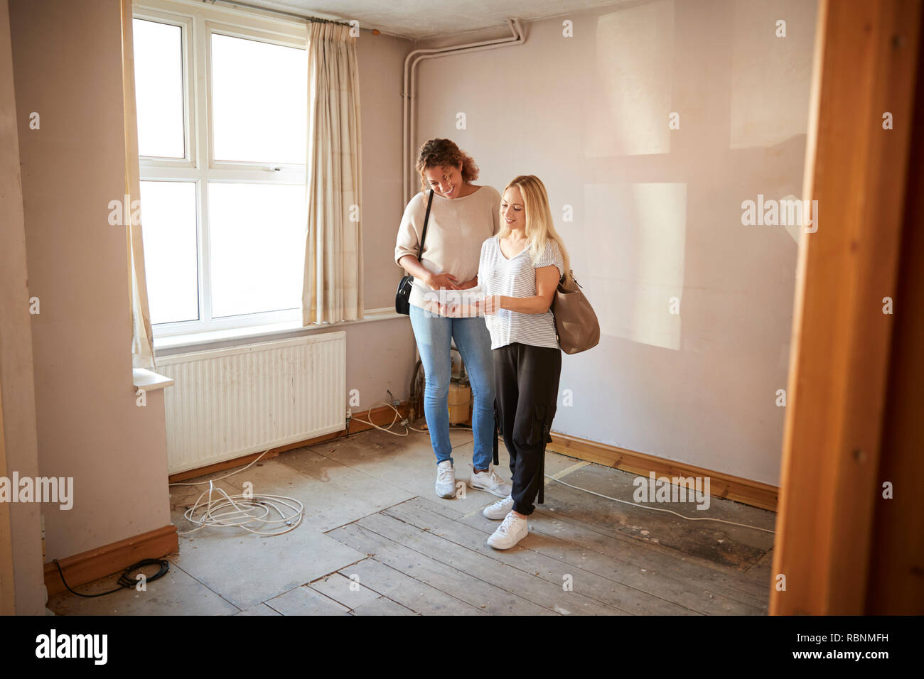 Two Female Friends Buying House For First Time Looking At House Survey In Room To Be Renovated Stock Photo