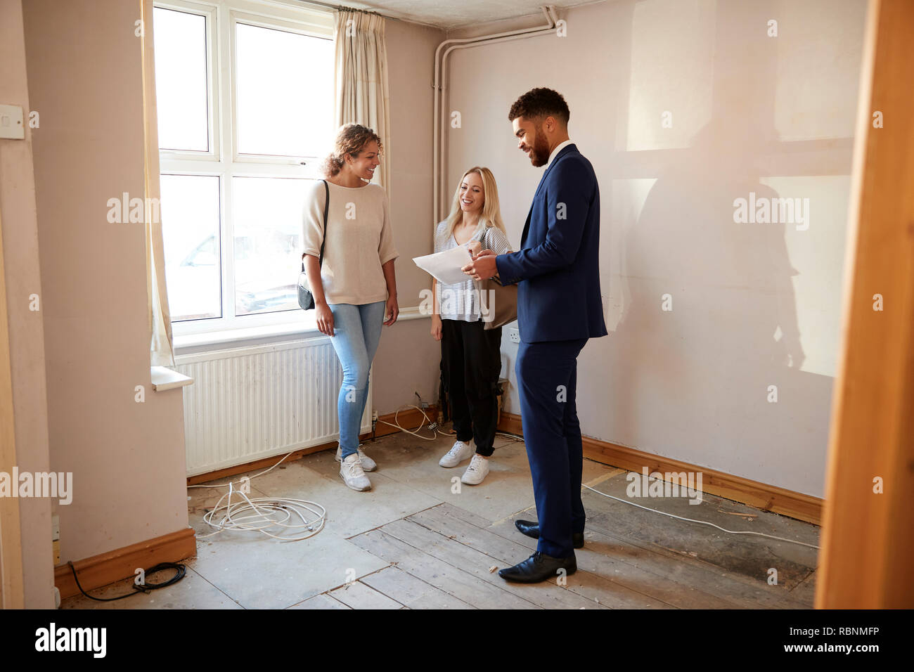 Two Female Friends Buying House For First Time Looking At House Survey With Realtor Stock Photo