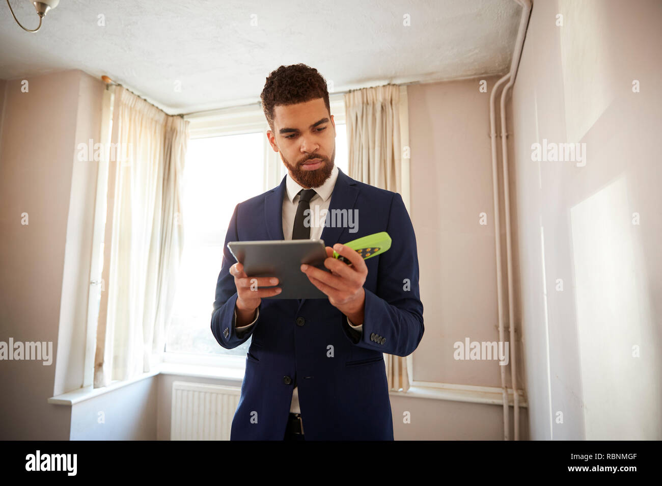 Male Realtor With Digital Tablet Measuring Room With Laser Measure Stock Photo