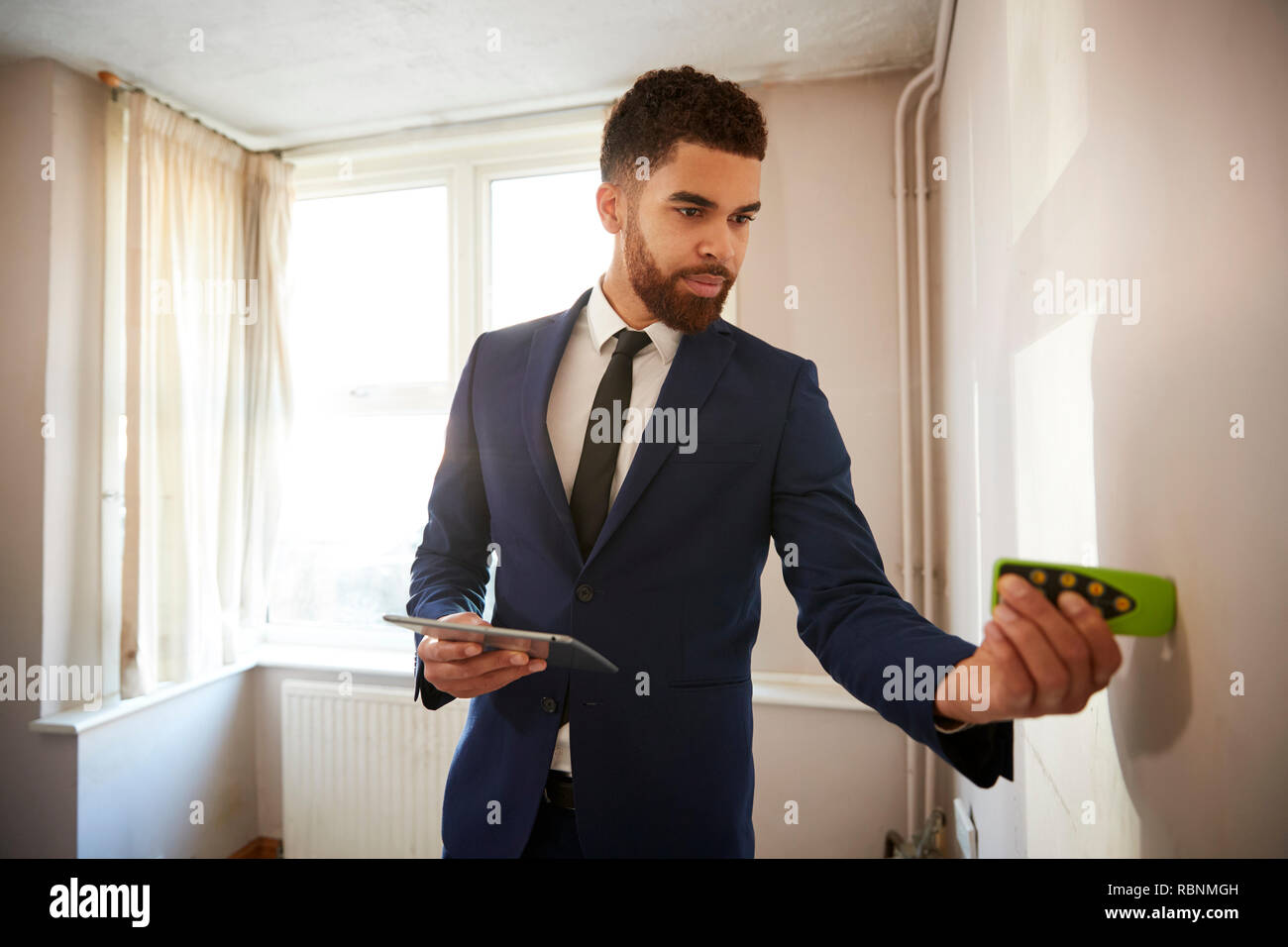 Male Realtor With Digital Tablet Measuring Room With Laser Measure Stock Photo