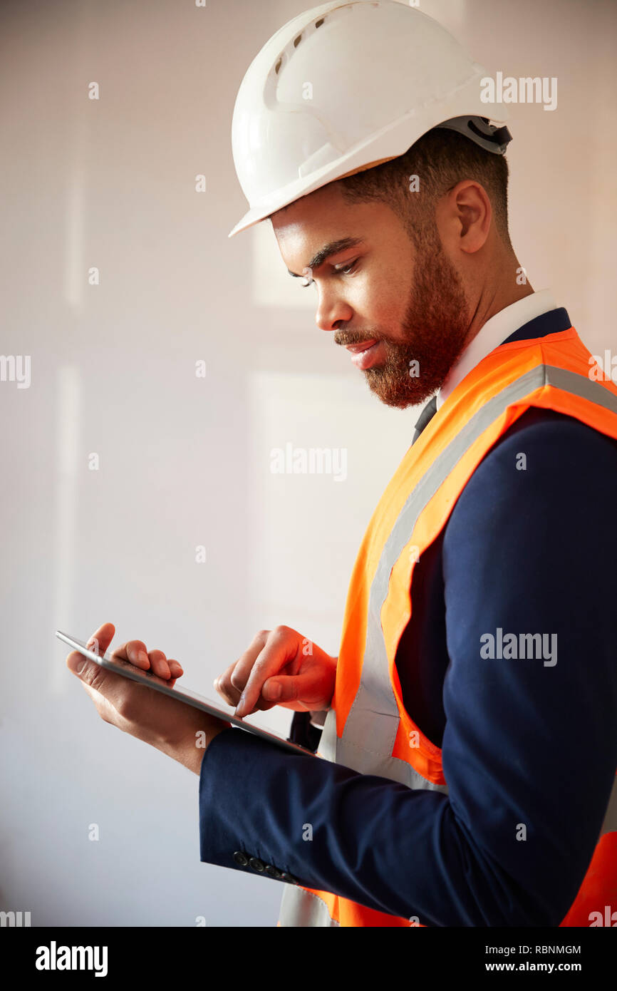 Surveyor In Hard Hat And High Visibility Jacket With Digital Tablet Carrying Out House Inspection Stock Photo