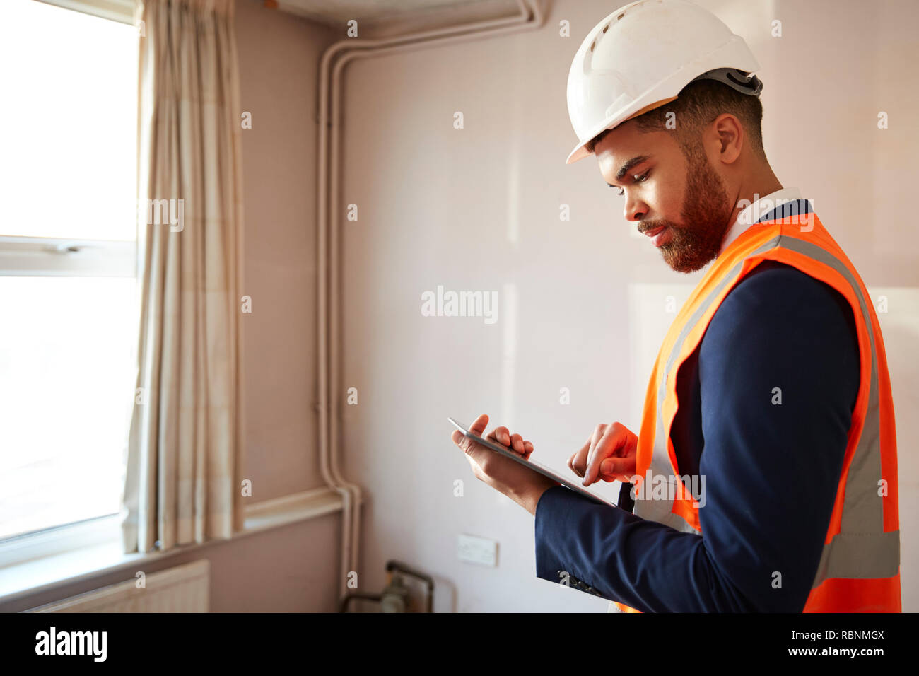 Surveyor In Hard Hat And High Visibility Jacket With Digital Tablet Carrying Out House Inspection Stock Photo