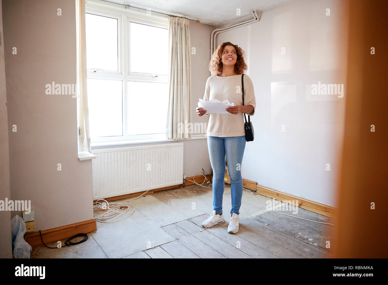Female First Time Buyer Looking At House Survey In Room To Be Renovated Stock Photo