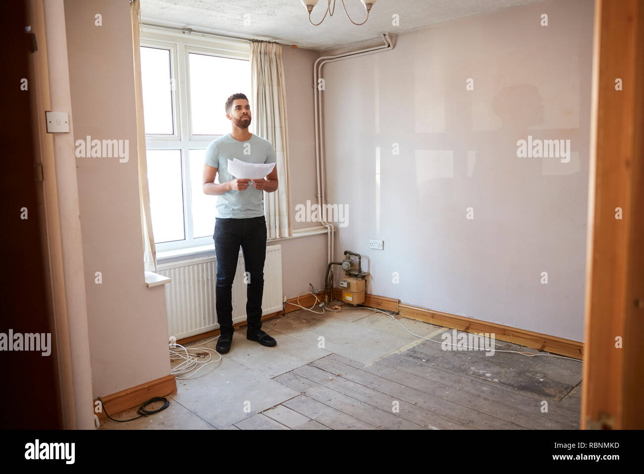 Male First Time Buyer Looking At House Survey In Room To Be Renovated Stock Photo