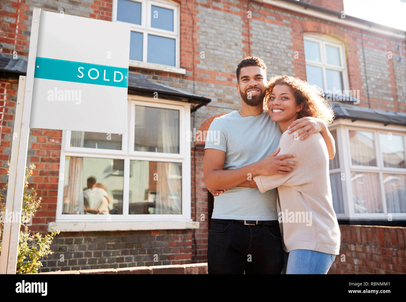 Portrait Of Excited Couple Standing Outside New Home With Sold Sign ...
