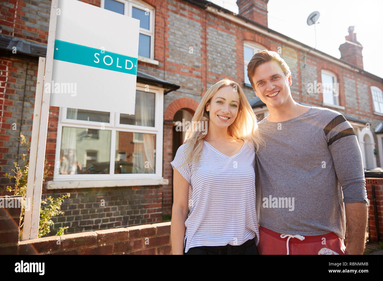 Portrait Of Excited Couple Standing Outside New Home With Sold Sign Stock Photo