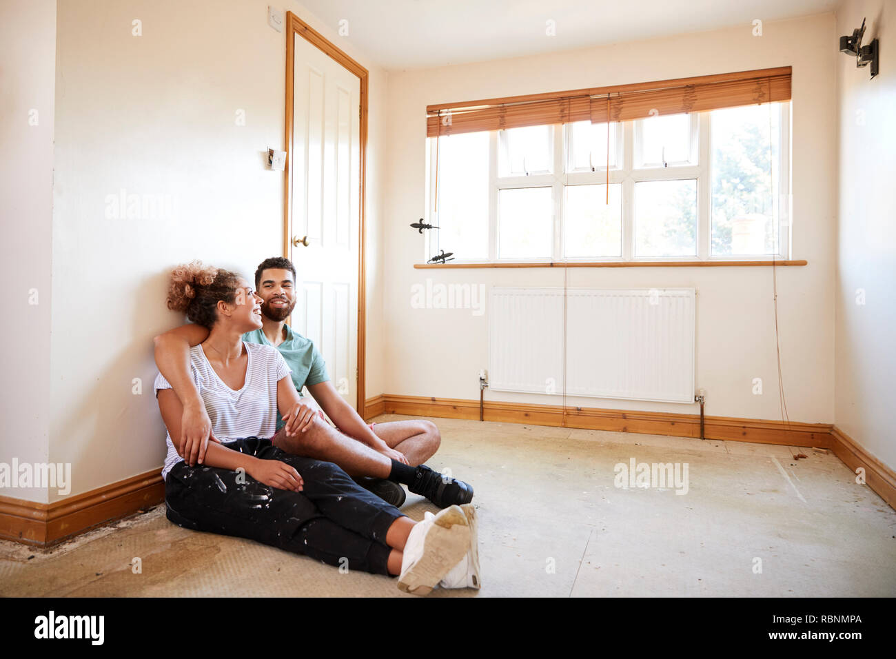 Couple Sitting On Floor In Empty Room Of New Home Planning Design Stock Photo