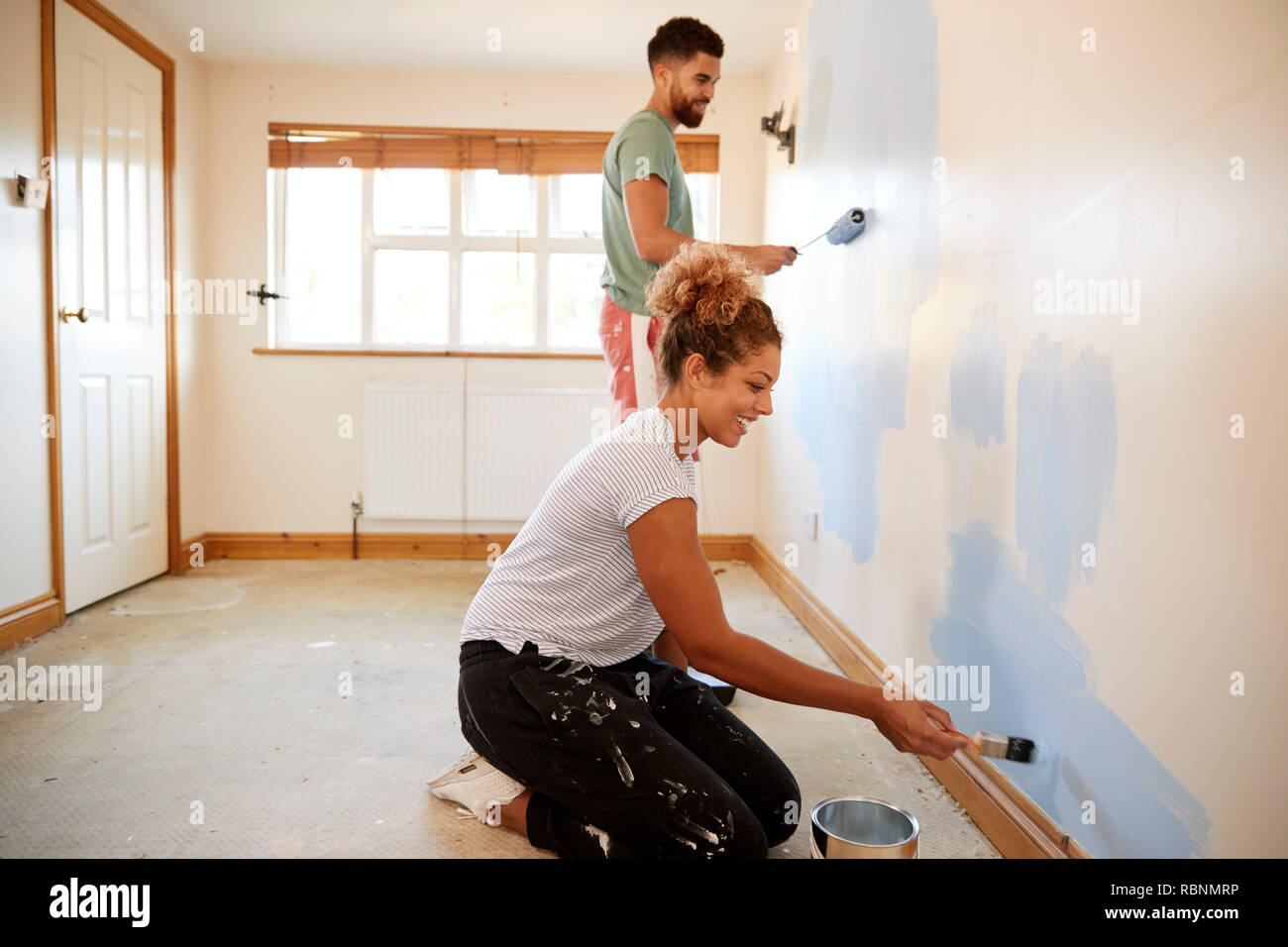 Couple Decorating Room In New Home Painting Wall Together Stock Photo