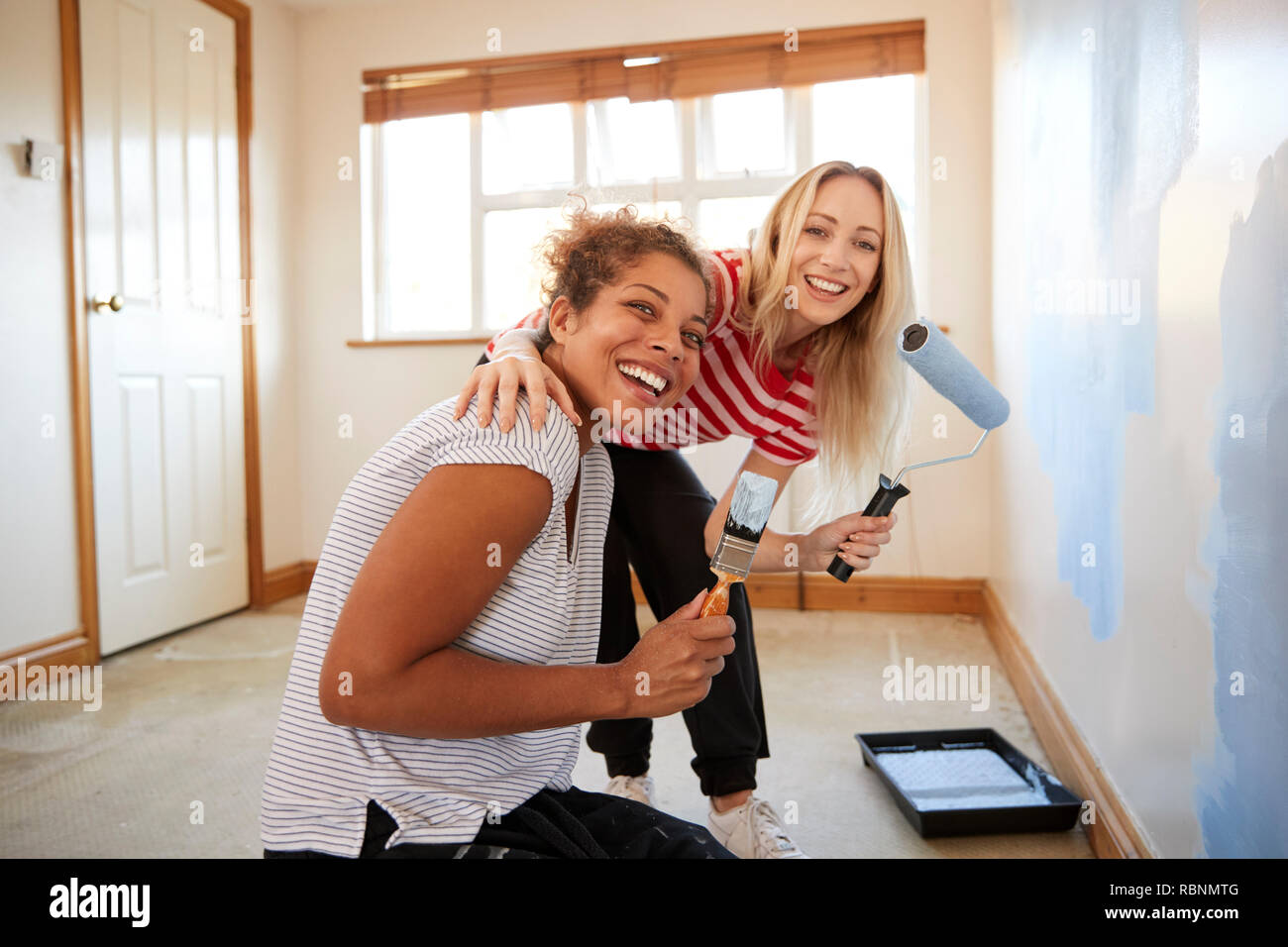 Portrait Of Two Women Decorating Room In New Home Painting Wall Stock Photo