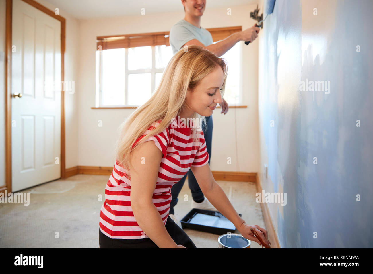 Couple Decorating Room In New Home Painting Wall Together Stock Photo