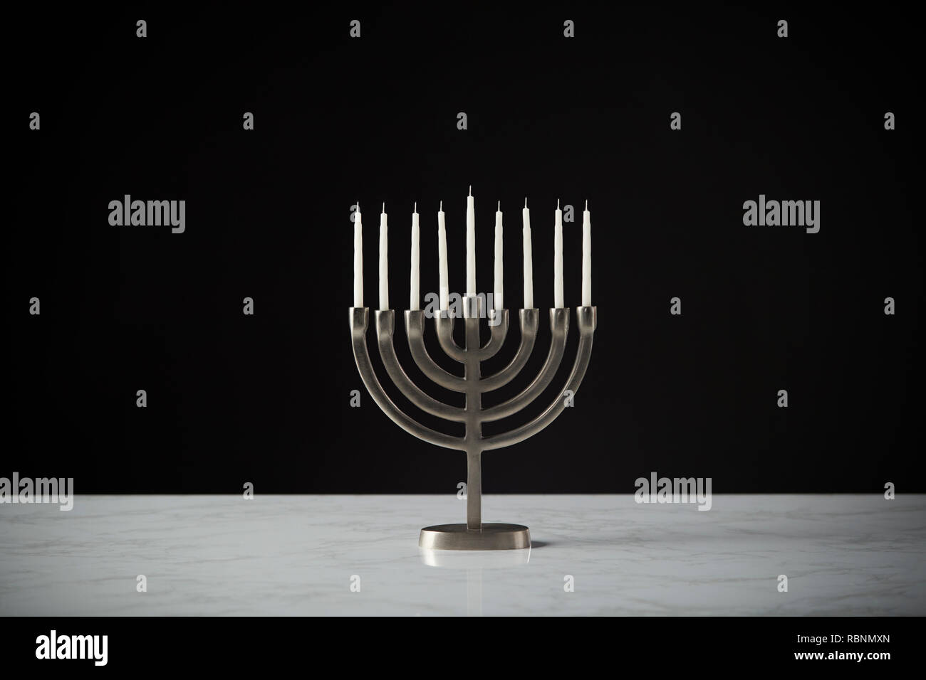 Metal Hanukkah Menorah With Unlit Candles On Marble Surface Against Black Studio Background Stock Photo