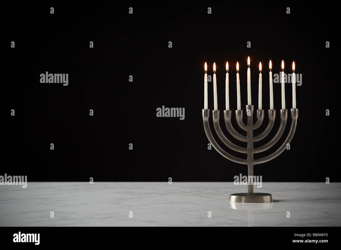 Lit Candles On Metal Hanukkah Menorah On Marble Surface Against Black Studio Background Stock Photo