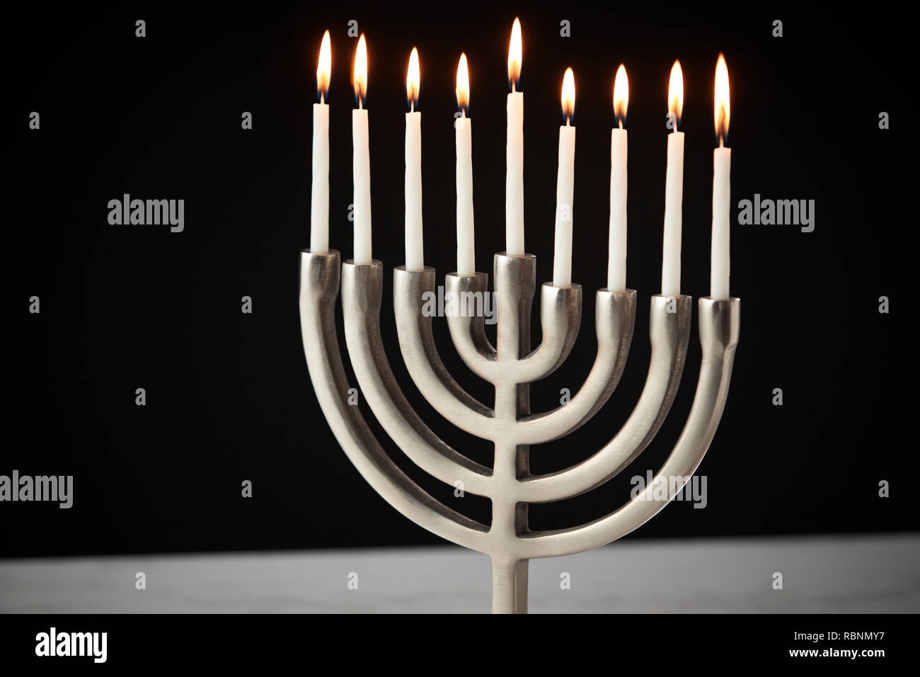 Lit Candles On Metal Hanukkah Menorah On Marble Surface Against Black Studio Background Stock Photo