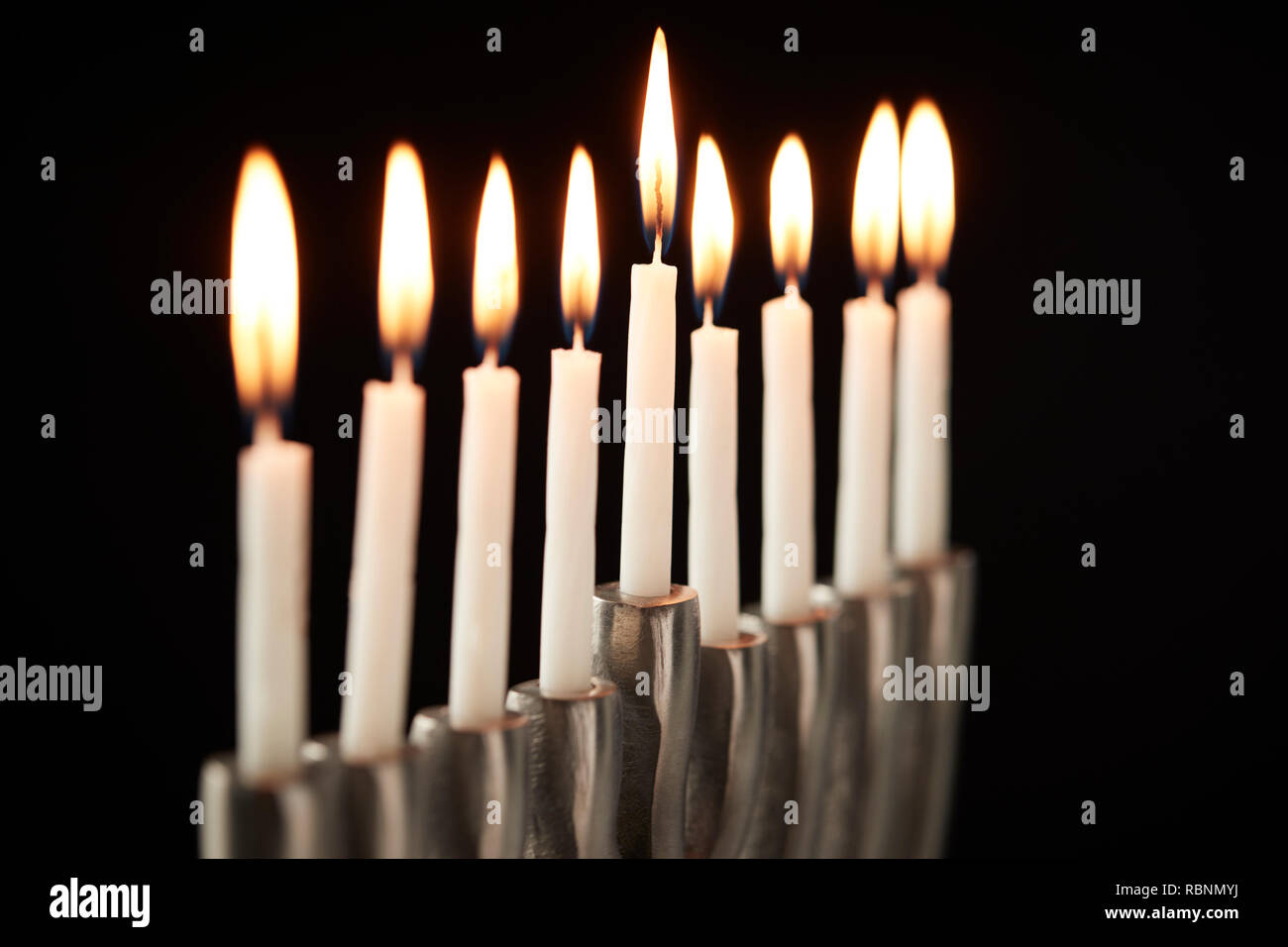 Close Up Of Lit Candles On Metal Hanukkah Menorah Against Black Studio Background Stock Photo
